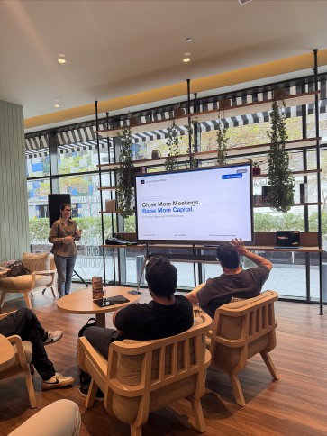 A speaker presents to founders beside a screen reading Close More Meetings. Raise More Capital.